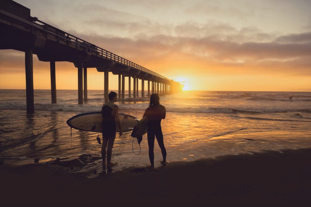 a couple of people holding surfboards on a beach with a pier in the background
